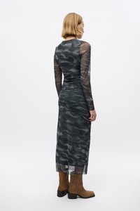 Long, fitted dress in a dark, wavy pattern with sheer long sleeves and a tapered silhouette. Paired with brown suede ankle boots.