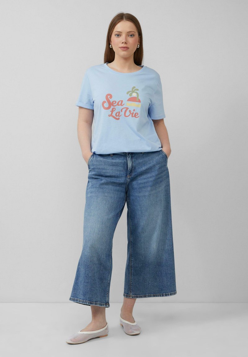 Lichtblauw katoenen t-shirt met 'Sea La Vie' grafiek, gecombineerd met wijde denim jeans en witte mesh ballerina's. Eenvoudig design en casual pasvorm.