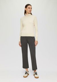Pull en col roulé beige, ajusté, en matière douce ; associé à un pantalon droit gris et des baskets blanches imposantes avec des accents taupe.