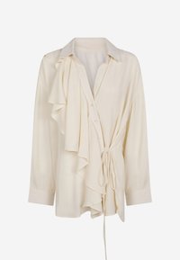 Blusa cremosa con maniche lunghe, dettaglio arricciato a sinistra, chiusura con bottoni e fiocco in vita. Tessuto morbido e testurizzato, design con colletto.