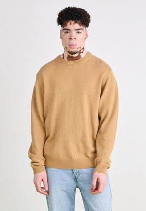 Pulover cu guler rotund, de culoare bej, dintr-o țesătură moale din amestec de lână, cu manșete și tiv cu nervuri; asortat cu blugi de culoare albastru deschis. Textură fină, croială lejeră.