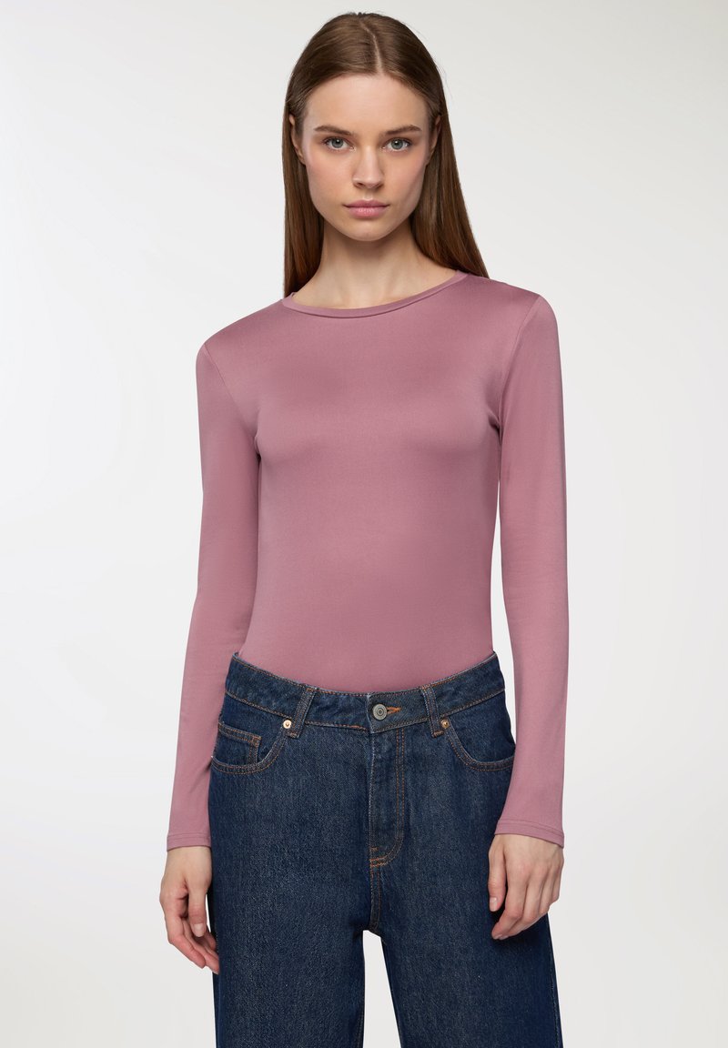 Długosleeve body z miękkiego różowego materiału, z okrągłym dekoltem. W połączeniu z ciemnoniebieskimi spodniami z wysokim stanem, podkreślonymi pomarańczowymi szwami.