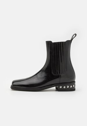 Bottines en cuir noir avec une finition brillante, panneaux latéraux élastiques, bout carré et clous décoratifs sur le talon.