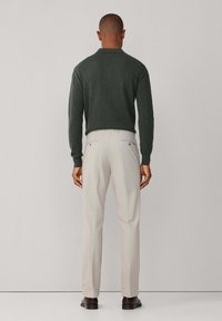 Suéter de manga larga verde oscuro, pantalones beige y zapatos oscuros, vistos desde atrás sobre un fondo liso.