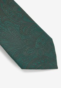 Cravate verte texturée présentant des motifs en paisley tissés avec des détails complexes, se rétrécissant vers une extrémité pointue.