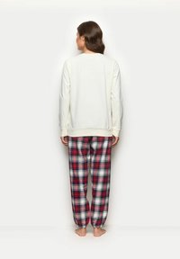 Jasnokremowa koszula z długim rękawem w połączeniu z luźnymi czerwono-granatowymi spodniami w kratę, z elastycznymi mankietami i paskiem w talii.