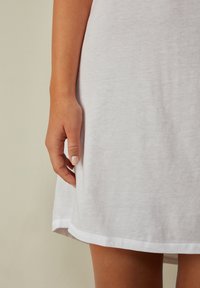 Abito bianco a maniche corte realizzato in un tessuto leggero e leggermente strutturato. Presenta un orlo curvo e cuciture tono su tono lungo i bordi.