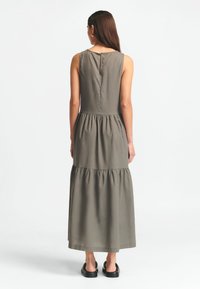 Tamsiai žalia, be rankovių maksi suknelė su keliais sluoksniais. Yra apvali iškirptė ir mygtukų užsegimas nugaroje. Lygus audinio paviršius.