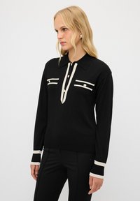 Maglione nero a maniche lunghe con colletto, caratterizzato da accenti crema, due strisce orizzontali sul petto e polsini a coste.