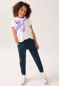 Lilla kõrge kaelusega kampsun heidetud valge t-särgi peale; mereväe sinised spordipüksid kummist mansetiga; valged tossud helkivate detailidega.