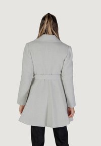 Cappotto a spina di pesce grigio chiaro con vita cinturata, maniche lunghe e orlo svasato. Realizzato in tessuto testurizzato, adatto per il clima più fresco.