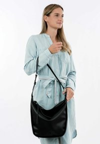 Borsa a spalla in pelle nera con una texture liscia e forma curva, dotata di chiusura con zip e manico regolabile.