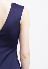 Robe bleu marine avec un dos en V profond, une texture douce et des détails en dentelle délicate le long des côtés. Fini en tissu lisse.