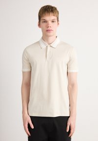 Cămașă polo cu mânecă scurtă în nuanță crem, cu guler și dungi contrastante. Are un logo subtil pe piept și un design cu croi clasic.