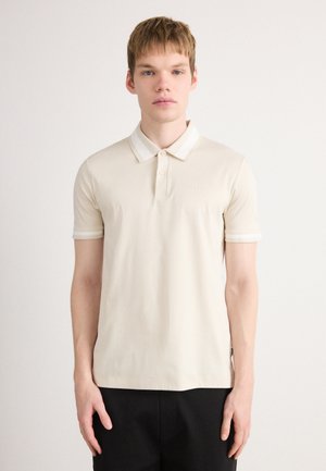 Polo à manches courtes en crème avec un col et des rayures contrastées. Présente un logo discret sur la poitrine et un design à coupe classique.
