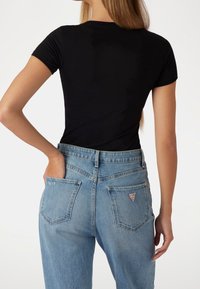 Zwarte slimfit t-shirt met korte mouwen, gecombineerd met lichtblauwe high-waisted jeans met een driehoeklogo op de achterzak.
