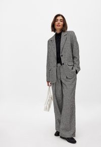 Textured gray and black tweed suit with a tailored blazer and wide-leg pants; paired with a black top and white handbag.