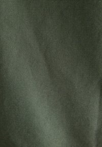 Dunkelgrüner Stoff mit einer strukturierten Webart, die ein einheitliches Muster und eine glatte Oberfläche aufweist, was auf ein strapazierfähiges Material hindeutet.