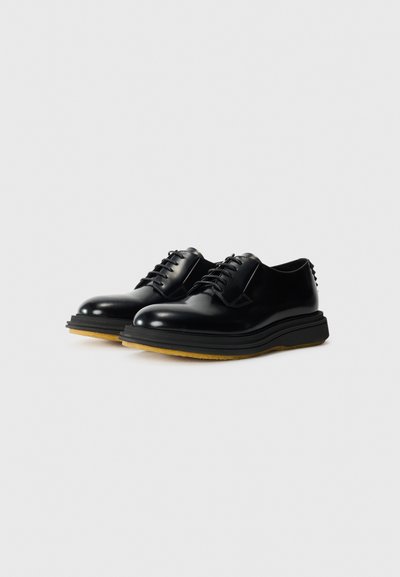 Black leather shoes with a glossy finish, rounded toe, and thick black sole. Features traditional lacing and minimalistic design accents.