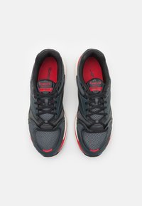 Zapatillas deportivas en negro y gris con material de malla, detalles en rojo y suela acolchada. Cuenta con cordones y plantillas con marca.