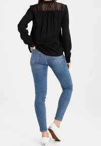 Maglietta nera a maniche lunghe con dettagli in pizzo sulla spalla, abbinata a jeans skinny blu e sneakers bianche. Tessuto morbido e vestibilità slim.