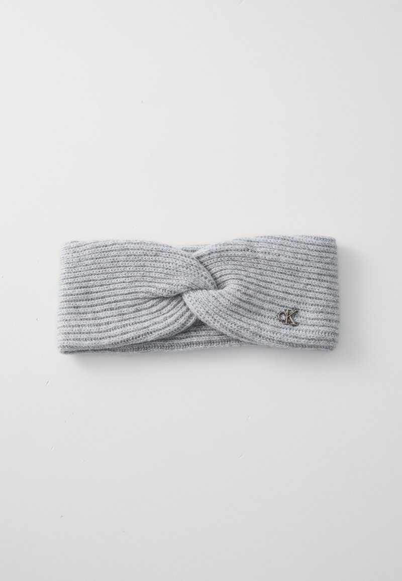 Un bandeau en tricot gris avec un design torsadé à l'avant et un petit logo en métal. Texture douce avec des détails côtelés.