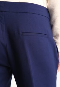 Mörkblå byxor med en slät yta, som har en diskret bakficka och rak passform, i kombination med en ljusfärgad, texturerad tröja.