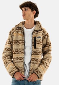 Giacca in fleece morbido, beige e marrone con motivo sfocato, dotata di zip frontale, collo alto e tasca sul petto con zip nera. Texture morbida in tutto il capo.