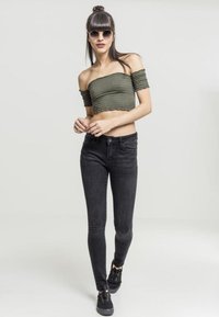 Olivenfarget av-knapp-kort topp med ribbet tekstur, sammen med svarte smale jeans og svarte snøring sko. Runde solbriller inkludert.