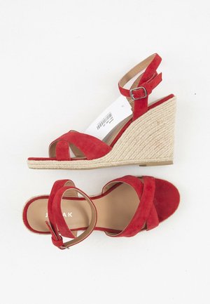 Røde ruskinds kilehæle med ankelremme og juteindpakkede hæle, én sko set fra siden og den anden ovenfra på hvid baggrund.