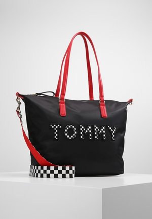 Czarna torba typu tote z czerwonymi uchwytami, napis "TOMMY" w kratkę oraz odpinany pasek w kratkę.