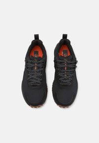Baskets de sport noires avec un tissu texturé et des superpositions synthétiques, mettant en valeur des lacets réfléchissants et une semelle intérieure orange. Design bas.