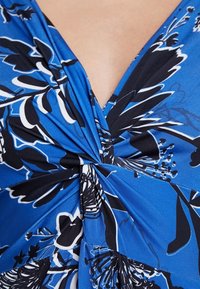 Tessuto blu con motivo floreale nero e bianco arricciato al centro, creando un dettaglio arricciato e un profondo scollo a V.