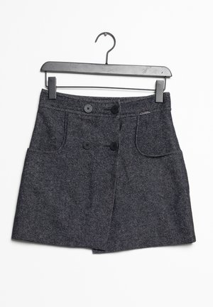 Falda de tweed gris con forma acampanada, dos bolsillos frontales y cierre de doble botón, colgando de una percha de alambre negra.