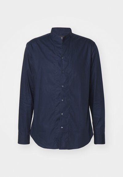 Temno modra majica z dolgimi rokavi z visokim ovratnikom, spredaj na gumbe, z gladko teksturo. Oznaka s majhno nalepko je znotraj ovratnika.