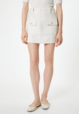 Witte tweed mini-jurk met twee voorzakken en gouden knoopaccenten. Soepele textuur, op maat gemaakte pasvorm en gestructureerde silhouet.