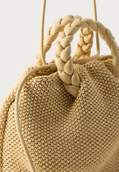 Μπεζ υφασμάτινη τσάντα χειρός με παχιά πλεγμένα δερμάτινα χερούλια και κλείσιμο με κορδόνι.