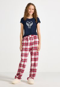 Navy short-sleeve T-shirt with winged graphic; red and white plaid pajama pants with an elastic waistband; cream-colored slippers.