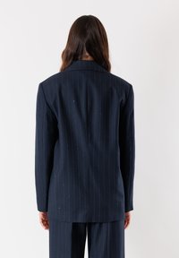 Blazer a righe navy realizzato in tessuto texturizzato, con spalline e rever a punta. Vestibilità sartoriale con uno spacco sul retro.