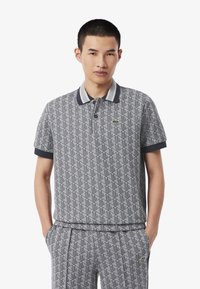 Polo grigia a motivo con maniche corte, caratterizzata da un colletto a righe e un piccolo logo. Il materiale sembra morbido e strutturato.