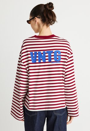 Dlouhý rukáv, pruhované tričko v červené a bílé barvě s modrým grafickým nápisem "VNTG." Volný střih, kulatý výstřih a široké rukávy.