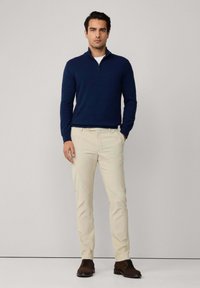 Suéter navy de cuello con cremallera, chinos crema y zapatos marrones. El suéter está hecho de una tela suave, y los pantalones tienen un corte ajustado.