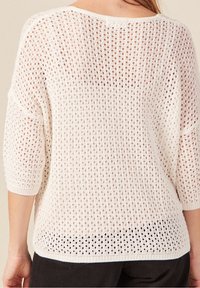 Bílý pletený svetr s volným střihem a otevřeným vzorem, se třičtvrtinovými rukávy a žebrovaným lemem. Lehký a texturovaný.