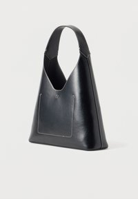 Sac à main en cuir noir avec une large bandoulière, des coutures blanches visibles et une poche plaquée à l'avant sur un fond clair uni.