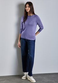 Ljuslila tröja med trekvartsärmar, tillsammans med mörkblå vida jeans och vita sneakers. Slät textur och avslappnad design.