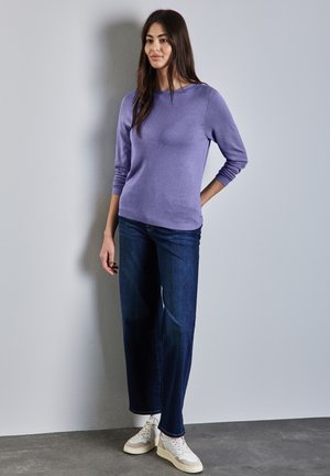 Maglione viola chiaro con maniche a tre quarti, abbinato a jeans a gamba larga blu scuro e sneakers bianche. Tessuto morbido e design casual.