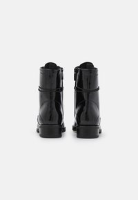 Botas negras hasta el tobillo en piel sintética brillante con un acabado suave, cremalleras laterales, un tacón bajo tipo bloque y detalles decorativos de correas alrededor del caño.
