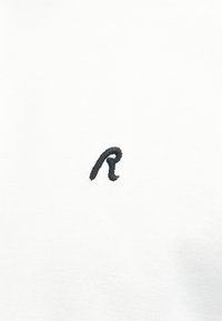 Lettre "r" minuscule noire brodée, centrée sur un fond de tissu blanc texturé.