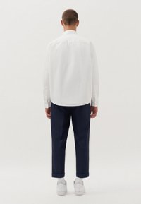 Camicia bianca a maniche lunghe con polsini a bottone, abbinata a pantaloni blu navy arrotolati e sneakers bianche. Design semplice, linee pulite e vestibilità classica.