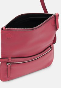 Czerwona skórzana torba na ramię o miękkiej fakturze, z zamknięciem na górze na zamek błyskawiczny, przednią kieszenią na zamek oraz regulowanym paskiem, co umożliwia różnorodne opcje noszenia.